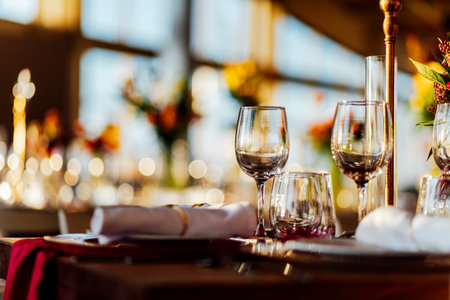 Elegant Christmas table setting with wine glasses and warm golden bokeh lights in a cozy restaurant atmosphere."の写真素材