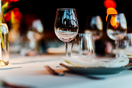 Elegant Christmas table setting with wine glasses and warm golden bokeh lights in a cozy restaurant atmosphere."の写真素材