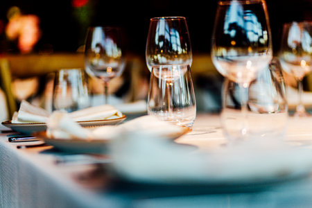 Elegant Christmas table setting with wine glasses and warm golden bokeh lights in a cozy restaurant atmosphere."の写真素材