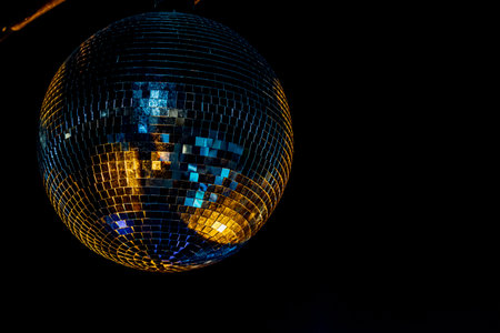 Crowd silhouettes dancing at night party with shiny disco ball and stage lights background.