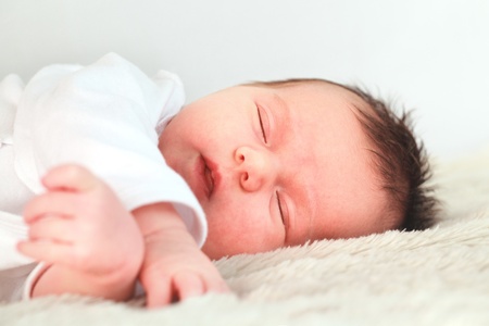 Newborn dark hair baby dressed in white is sleeping on the downy blanket close upの写真素材