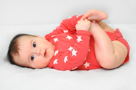 Nice baby with open blue eyes playing with her feets lying on the back