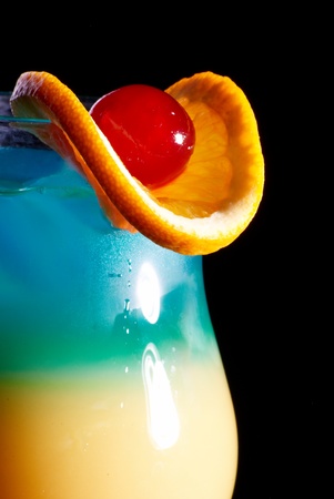 Colorful fresh cocktail in glass decorated with piece of orange and red cherryの写真素材