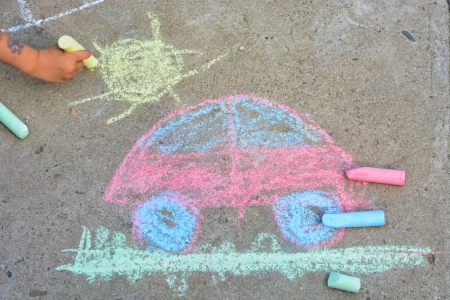 Child`s hand is drawing car, sunand grass  using colorful chalks on asphaltの写真素材