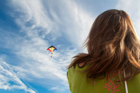 the girl starts colorful kite flying on the background of white clouds and blue sky