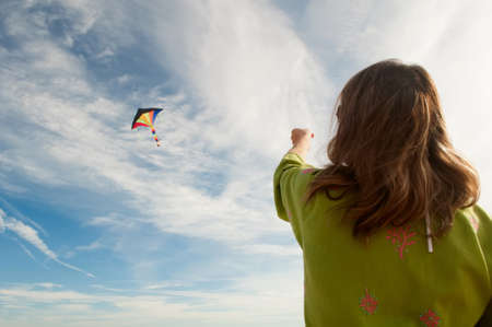 the girl starts colorful kite flying on the background of white clouds and blue sky