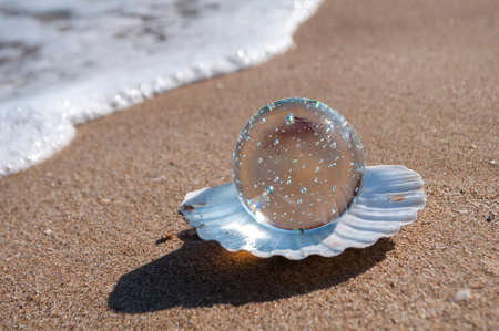 transparent crystal ball as the pearl lies in a seashell in the sand on the beachの写真素材