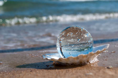 transparent crystal ball as the pearl lies in a seashell in the sand on the beachの写真素材
