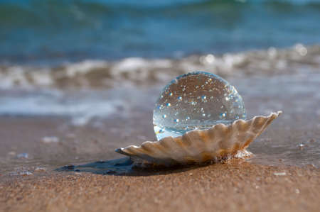 transparent crystal ball as the pearl lies in a seashell in the sand on the beachの写真素材
