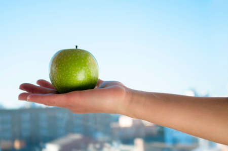 green apple in a female hand on the palm on the background of blue skyの写真素材