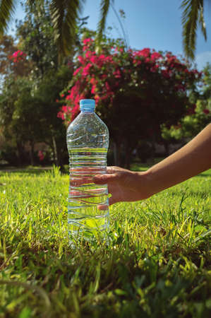 a simple bottle of mineral water stands on a background of green grass and trees in the sunshine.