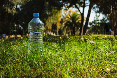 a simple bottle of mineral water stands on a background of green grass and trees in the sunshine.の写真素材