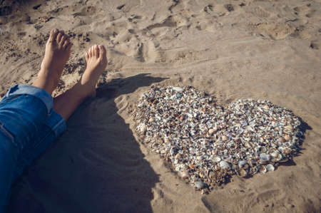 girls feet on the sand beside her lined with shells heart