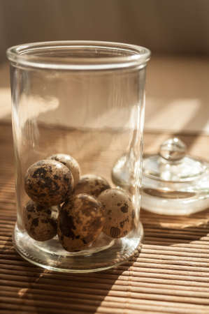 quail eggs in a decorative glass jar on the table in the sunの写真素材