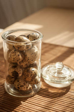 quail eggs in a decorative glass jar on the table in the sunの写真素材