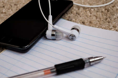 on a fluffy carpet phone with earphones and a notebook for notesの写真素材