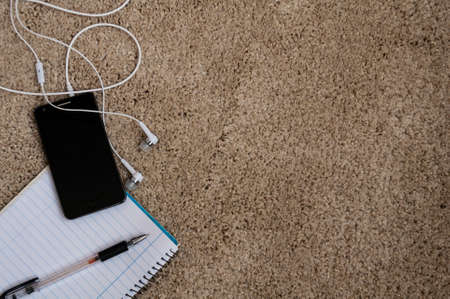 on a fluffy carpet phone with earphones and a notebook for notesの写真素材