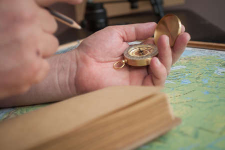 male hands holding a compass over the map and something is going to record in the notebookの写真素材