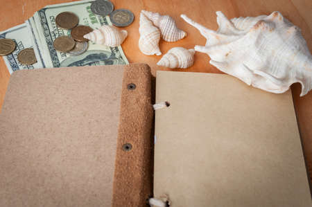 on a wooden table lies an open notebook, shells and money. planning a trip on vacationの写真素材