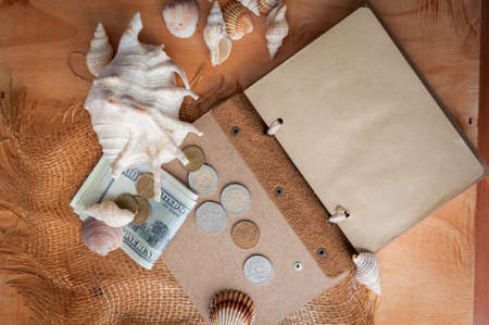 on a wooden table lies an open notebook, shells and money. planning a trip on vacation