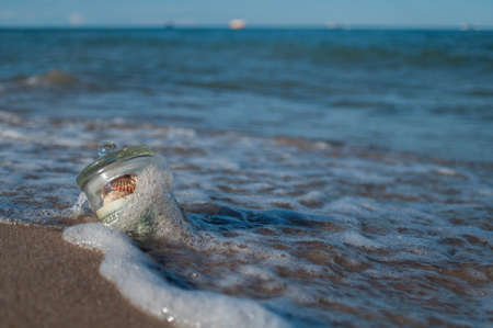 in the sand in the surf is the glass jar with money and shells, gift sea