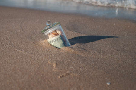 in the sand in the surf is the glass jar with money and shells, gift seaの写真素材