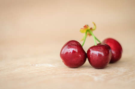 on a wooden surface are three ripe cherries