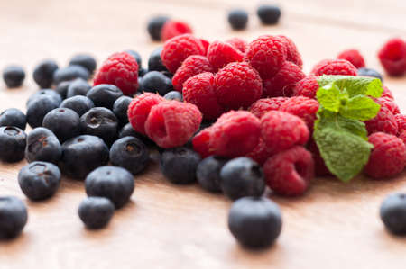 juicy raspberries and blueberries scattered on a wooden tableの写真素材