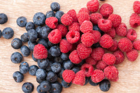juicy raspberries and blueberries scattered on a wooden tableの写真素材