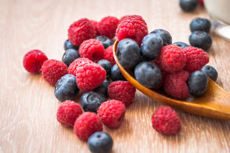 juicy raspberries and blueberries scattered on a wooden tableの写真素材