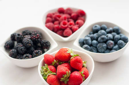 on a white background in white bowls of fresh, juicy wild berries blueberries raspberries strawberries and blackberries, delicious Supplement to any diet meals.の写真素材