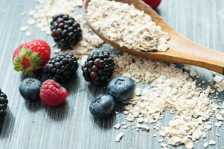 on the table, a scattering of raspberries blueberries blackberries and strawberries and a spoonful of cerealの写真素材