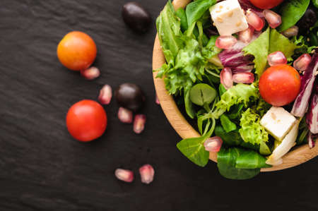 vegetarian food is salad, canonigo tomatoes olives pomegranate, and feta cheese. on a black backgroundの写真素材