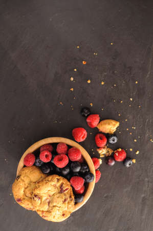 a few homemade cookies and raspberries and blueberries on black background