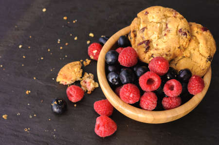 a few homemade cookies and raspberries and blueberries on black background