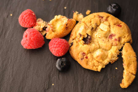 a few homemade cookies and raspberries and blueberries on black background