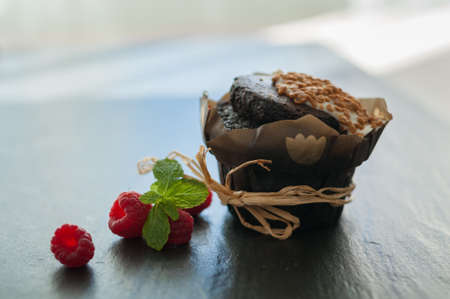 single chocolate muffin with nuts and raspberries on a black background