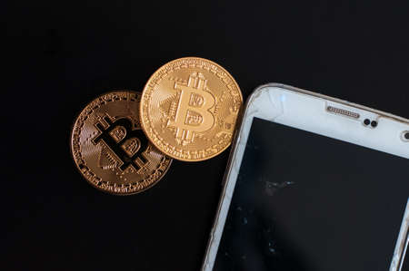 two golden coins of bitcoin and dollars and mobile phoneの写真素材