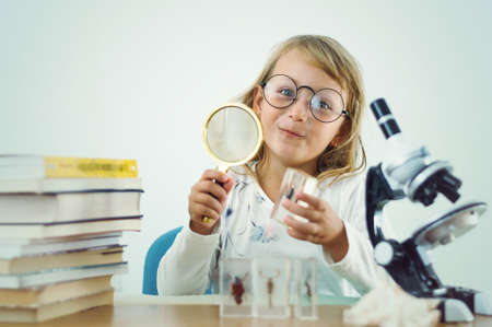little girl playing scientist among stacks of books with a microscope