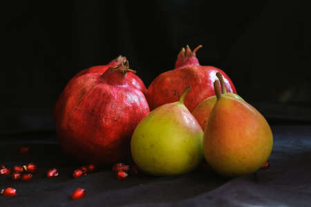 pomegranates and two pears on a dark background and with scattered pomegranate seeds aroundの写真素材