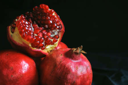 several ripe whole pomegranates and one broken on a dark backgroundの写真素材