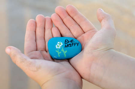 in childrens hands a decorated stone with the inscription be happyの写真素材
