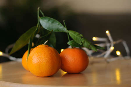 a few juicy and delicious tangerines on the table in the light of white garlandsの写真素材