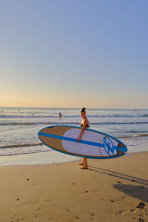 young beautiful girl in a bathing suit with a surfboard at dawnの写真素材