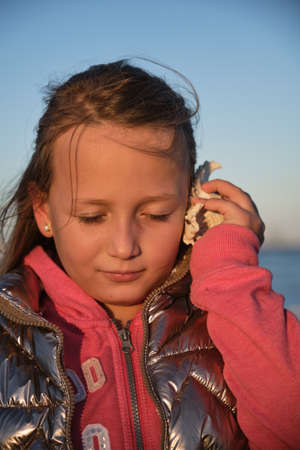 a girl listens to a seashell on the beach