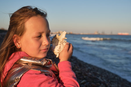 a girl listens to a seashell on the beachの写真素材