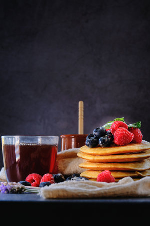 pancakes with berries and honey on dark background