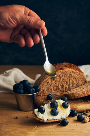 a piece of rusty bread with cream cheese and blueberries drizzled with honeyの写真素材