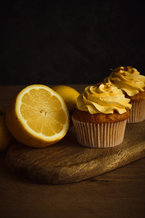 two lemon cakes next to slices of yellow lemon on a dark backgroundの写真素材