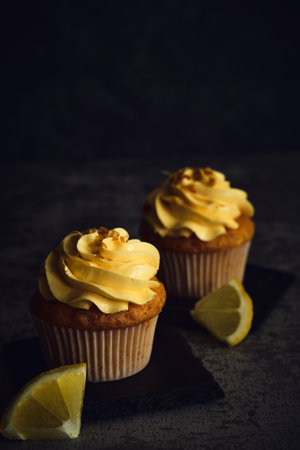 two lemon cakes next to slices of yellow lemon on a dark backgroundの写真素材